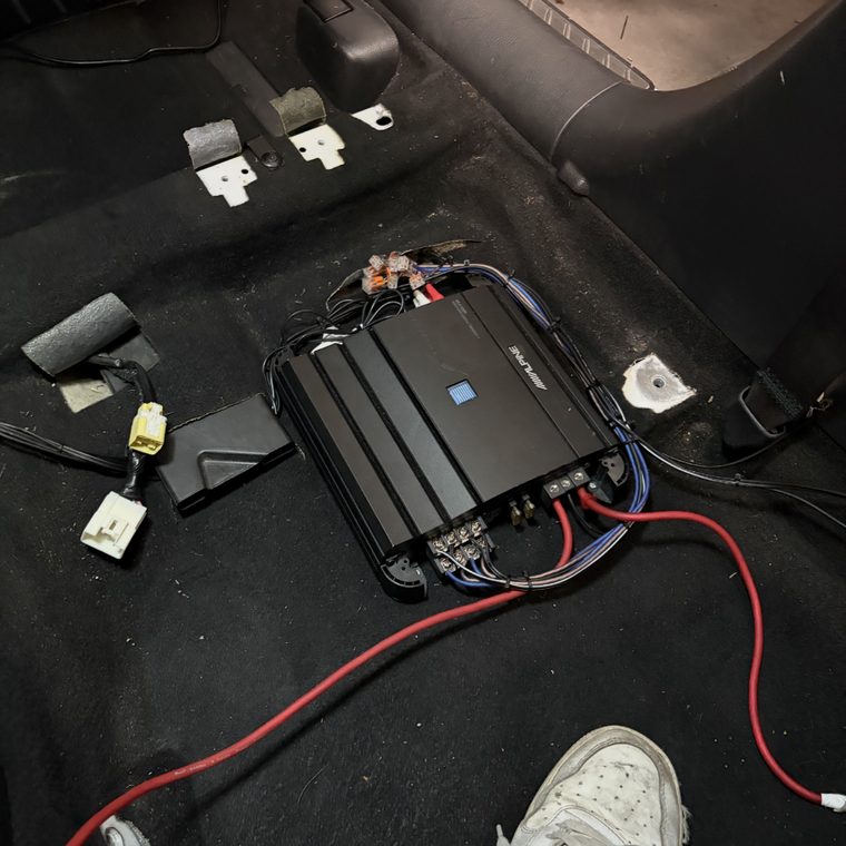 Car amplifier wired up on the boot floor with power, earth and speaker cable runs