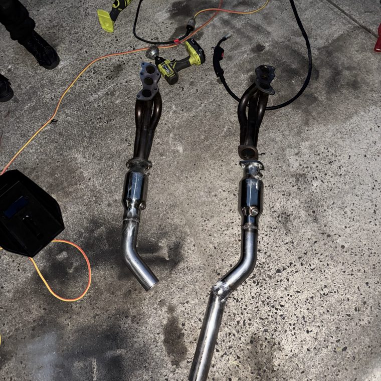 Pair of fabricated exhaust headers and pipes laid out on the driveway