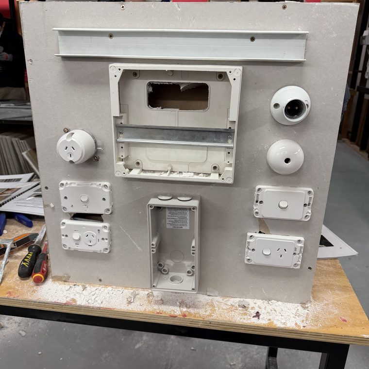 Plasterboard practice board fitted with switches, outlets, batten holders and a switchboard enclosure